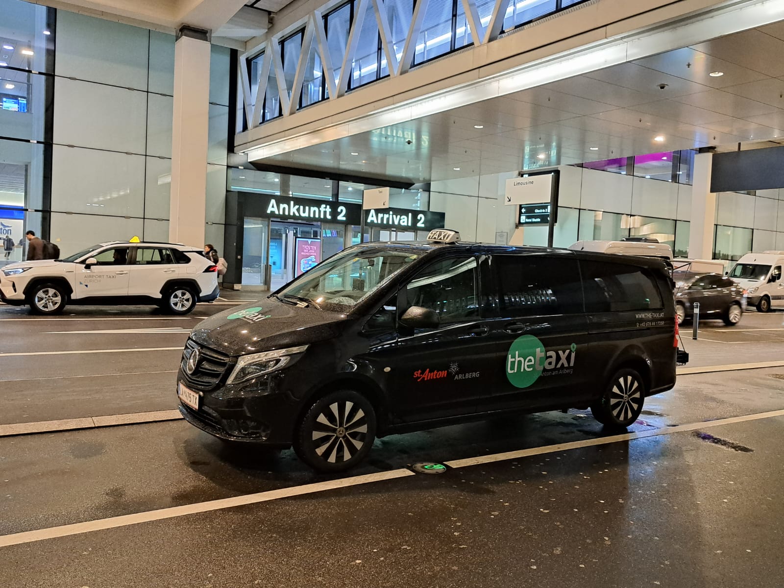Black taxi van parked in front of the Arrival 2 entrance at the airport, ready to pick up passengers.